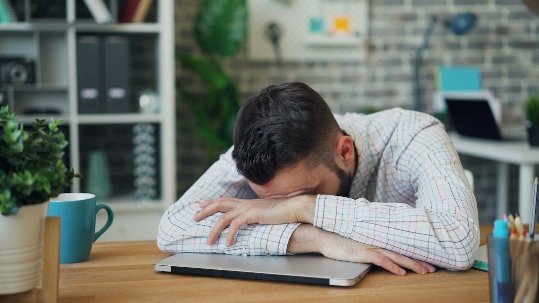 Tired man resting his head on folded arms beside a laptop