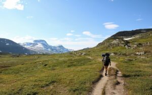 Hiker with a backpack follows a rugged mountain trail through alpine terrain