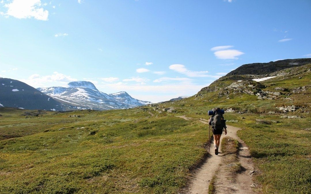 Hiker with a backpack follows a rugged mountain trail through alpine terrain
