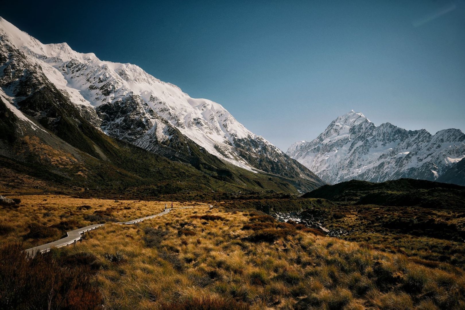Boardwalk track crossing tussock beneath snow-covered New Zealand mountains